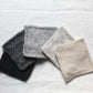 Five different marls knitted up in little squares, arranged on a white linen tablecloth.