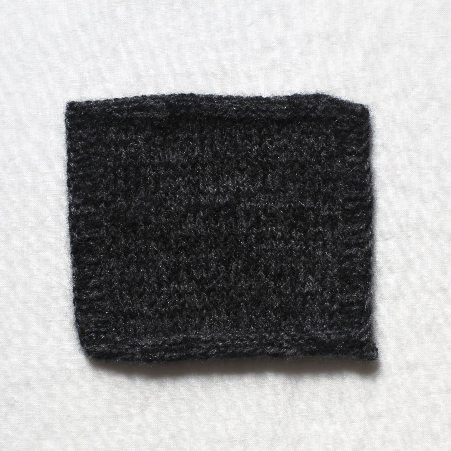 A small sample of black and dark grey yarns knitted to create a soft marl