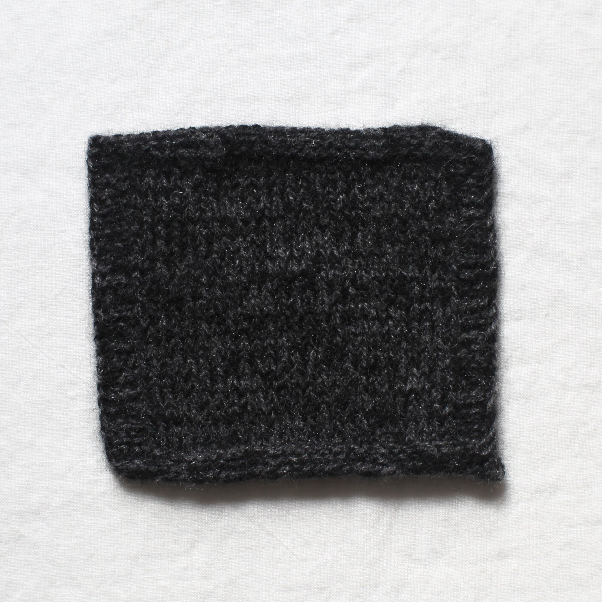 A small sample of black and dark grey yarns knitted to create a soft marl