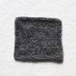 A knitted square from light and dark grey yarns to create a soft marl. The background is a white linen table cloth.