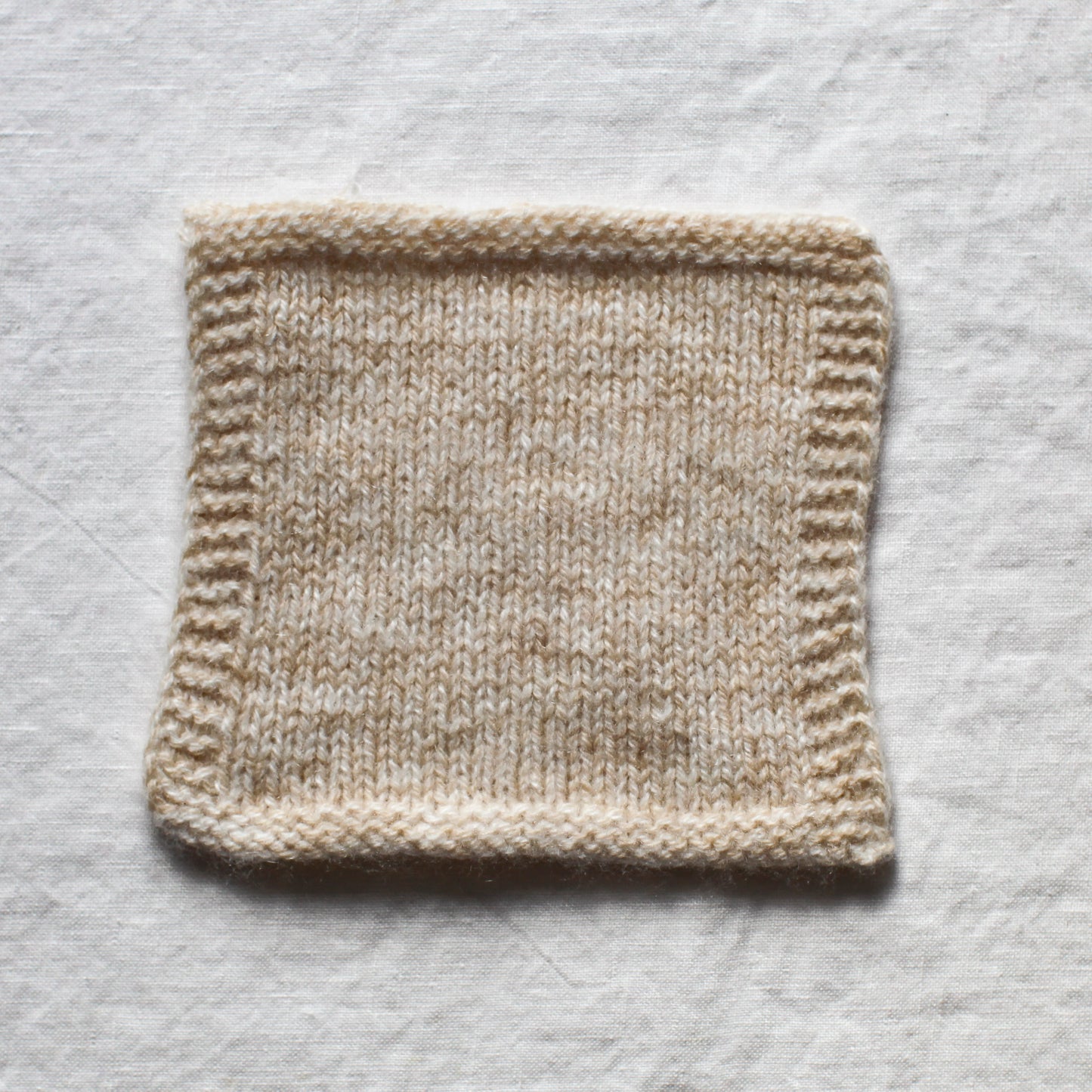 A knitted square using white and a soft brown cappucino coloured cashmere yarn creates a soft marl. The background is a white linen tablecloth.