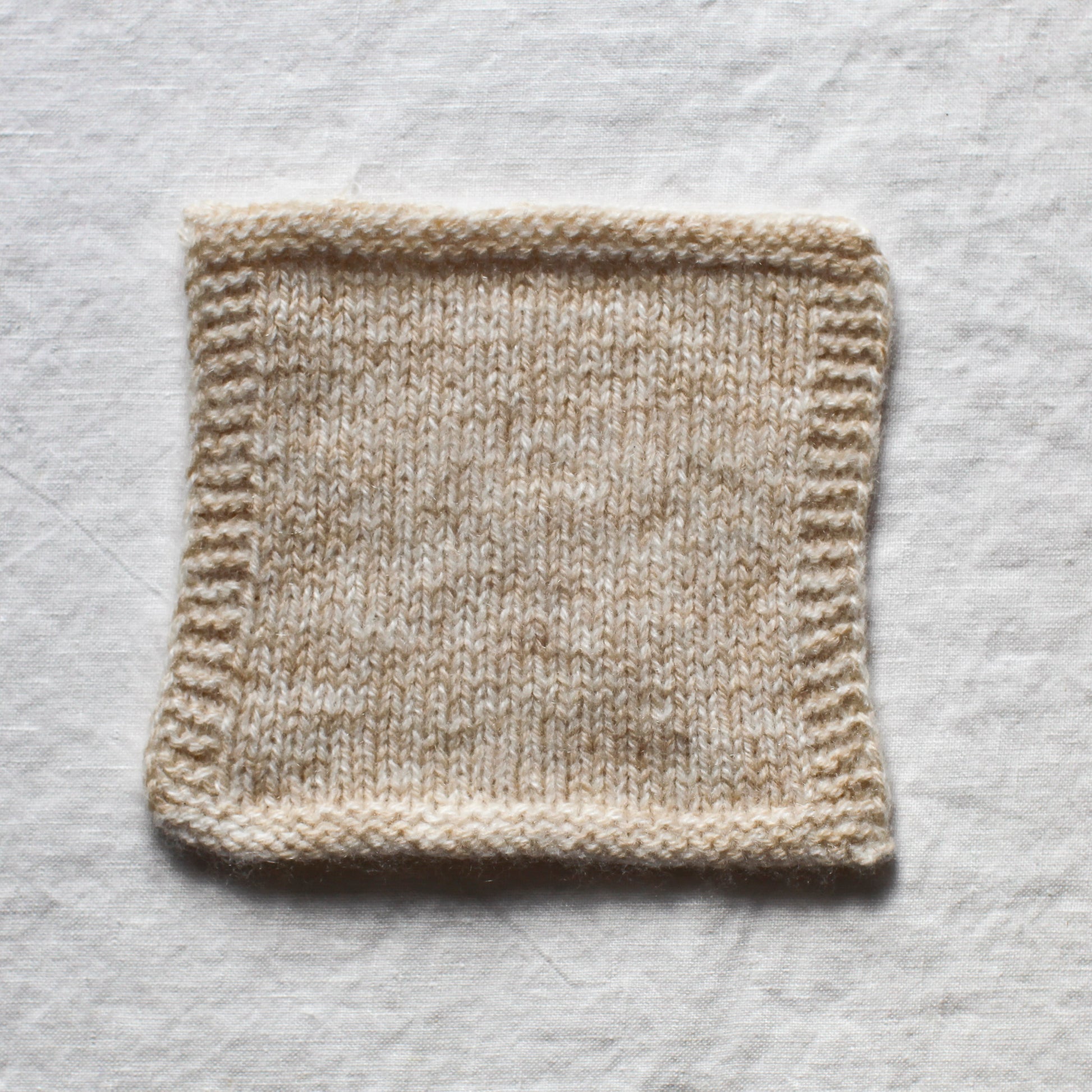 A knitted square using white and a soft brown cappucino coloured cashmere yarn creates a soft marl. The background is a white linen tablecloth.